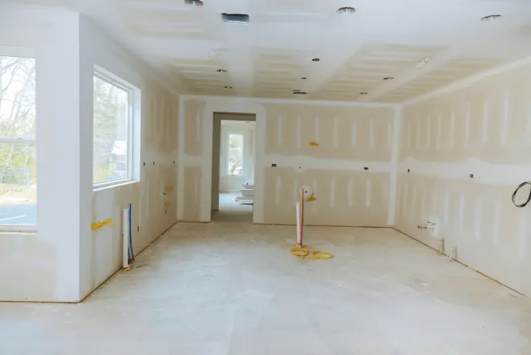 Interior construction reference showing a large room with installed drywall, window openings and unfinished floors.