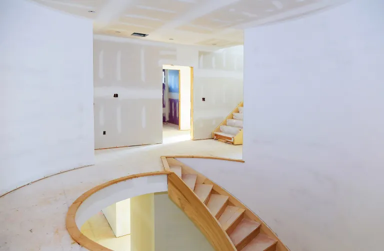 Unfinished interior with curved stair opening, timber framing and drywall ready for finishing.
