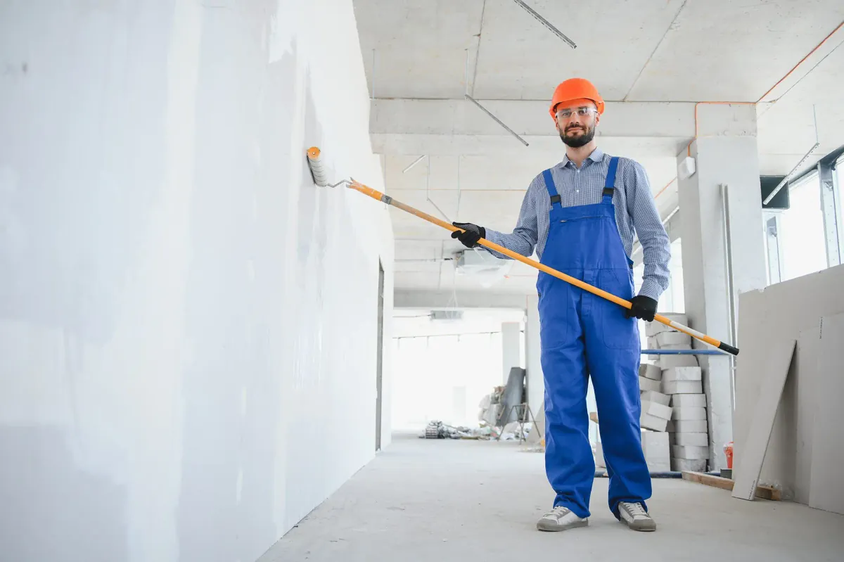 Painter with a roller beside a wall in an unfinished interior, illustrating related painting work.
