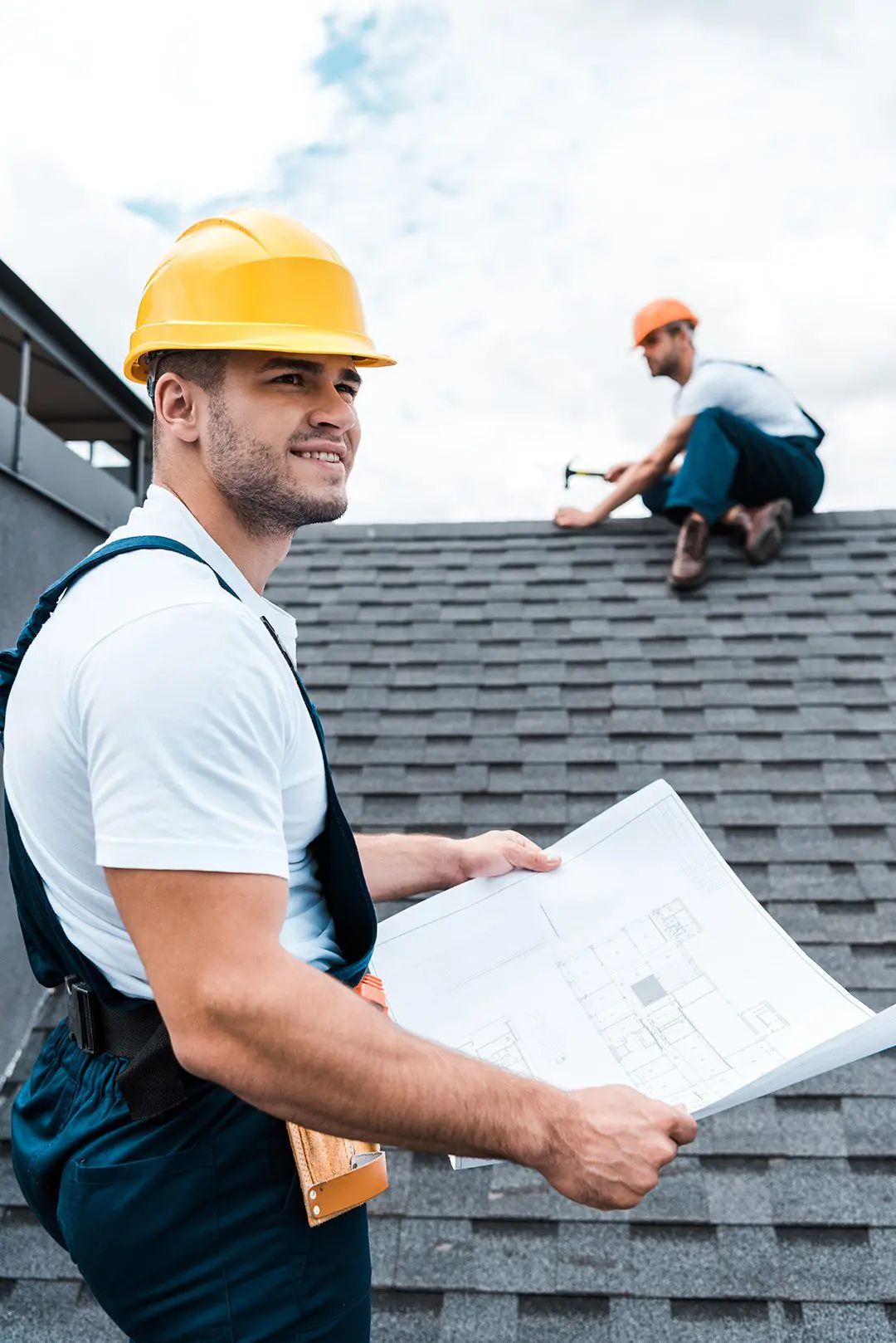 Real construction-reference photograph of a builder reviewing plans beside an active roof installation.