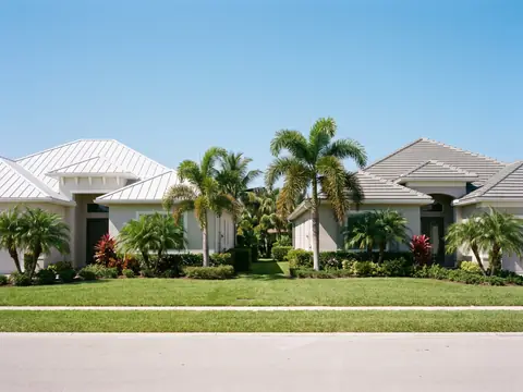 Two neighboring homes, one with a white metal roof and one with a gray tile roof