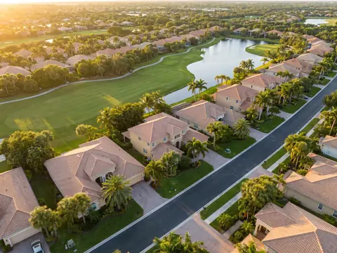 Aerial view of tile-roofed homes along a golf course and lake in Palm Beach Gardens