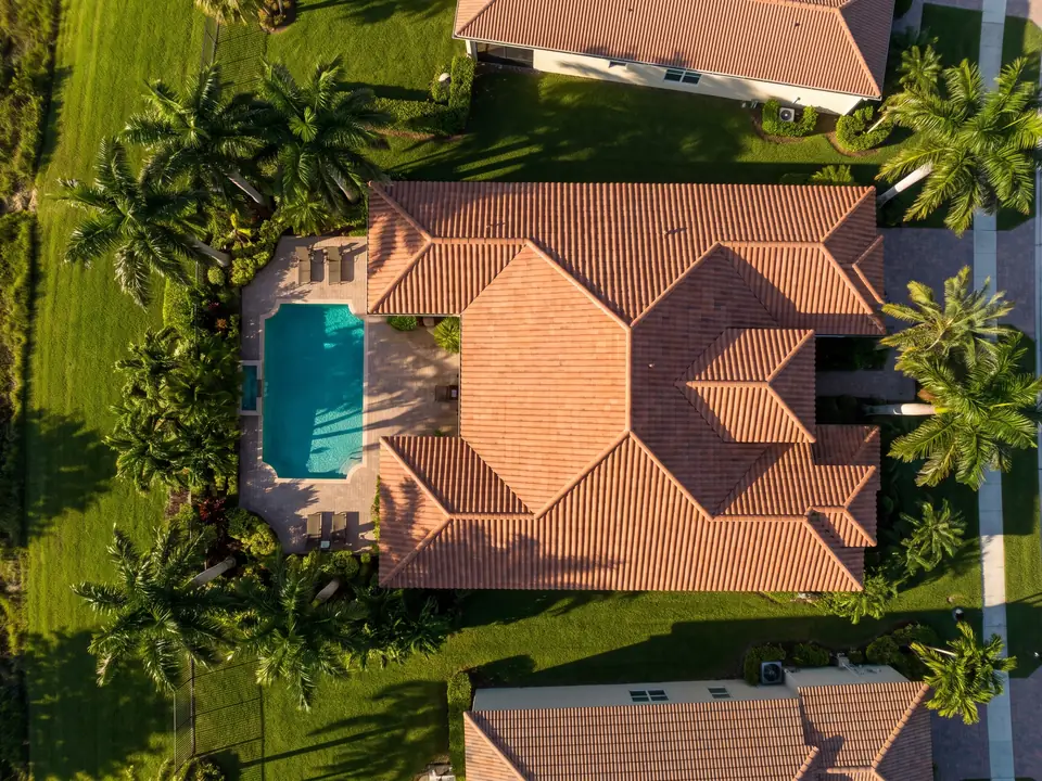 Overhead view of a terracotta tile hip roof beside a pool and palm trees