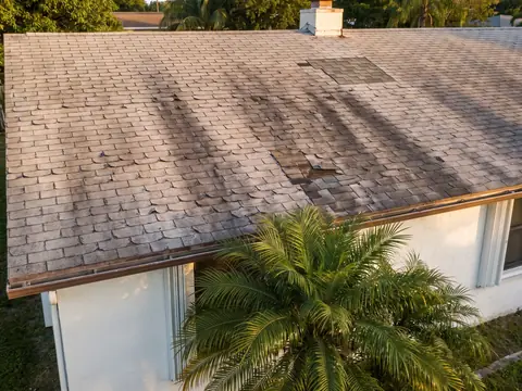 Worn, patched asphalt shingle roof on an older stucco home